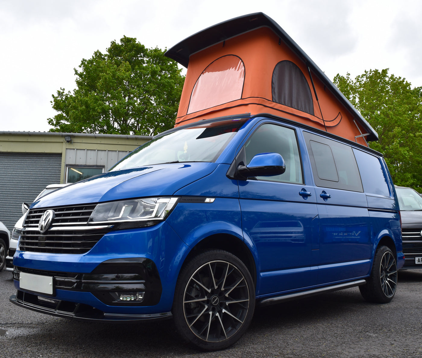 Blue Volkswagen van with an orange canvas Skyline pop top parked outdoors.