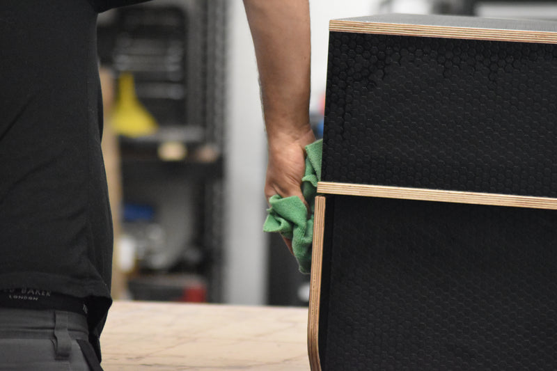 Person cleaning a black storage cabinet with a green cloth in a workshop setting