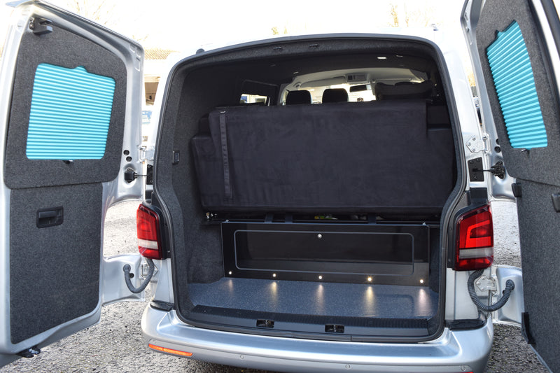 Van with rear doors open, showing a folded black bed or mattress inside.