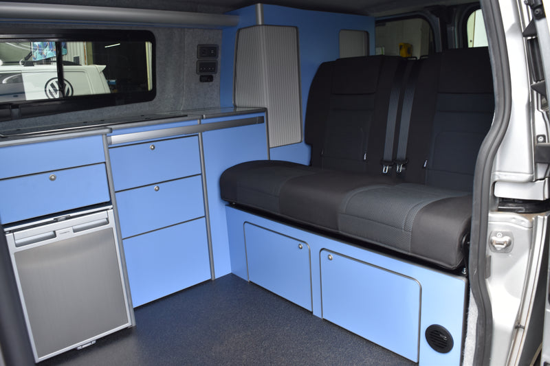 Van interior with black seats, blue cabinets, and a refrigerator.