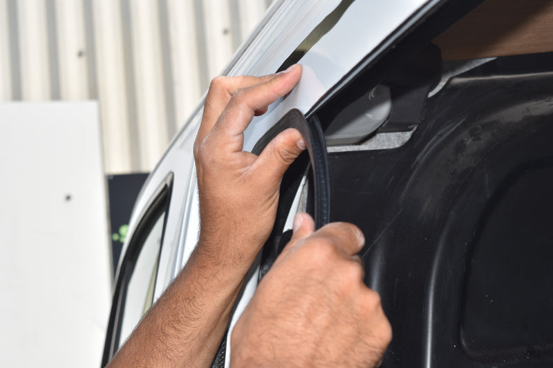 Person applying a metal trim on a van during glass window installation