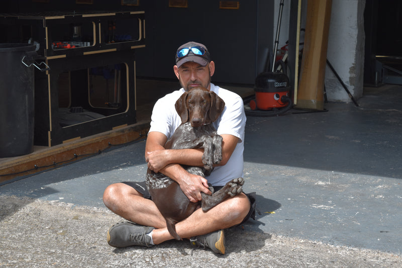 Man sitting on the ground holding a dog in a garage setting