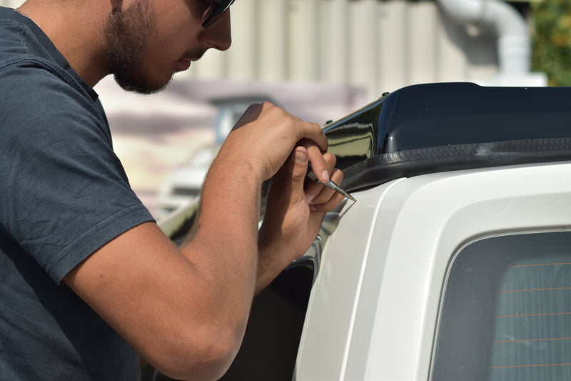 Person working on a vehicle, installing an awning rail using a metal punch to locate drilling point. 
