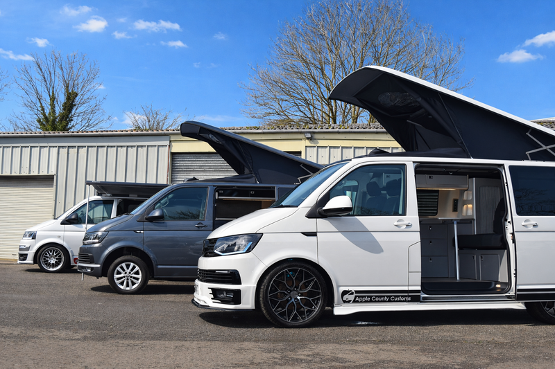 Three camper vans lined up in a row with pop tops raised
