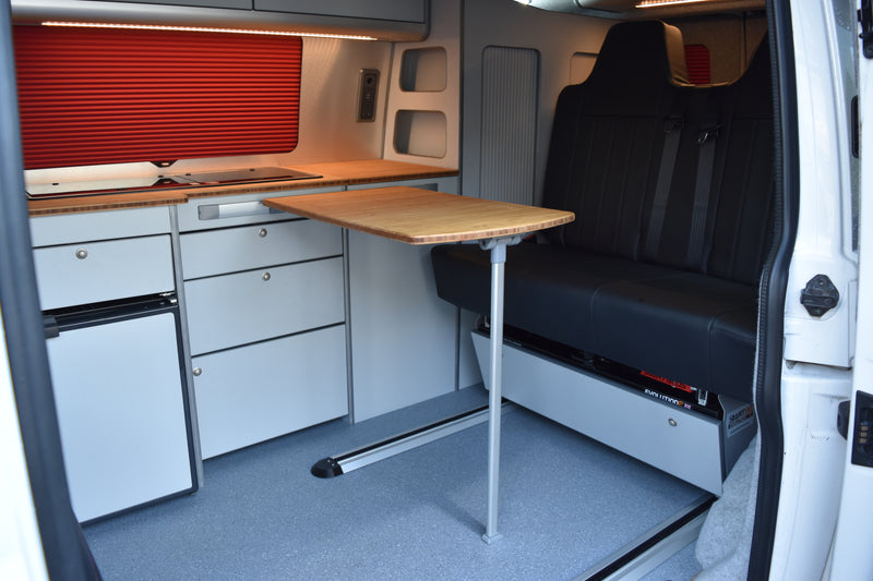 Van interior with a fold-out table, storage compartments, and a refrigerator with a Smart Bed Evo R rail bed