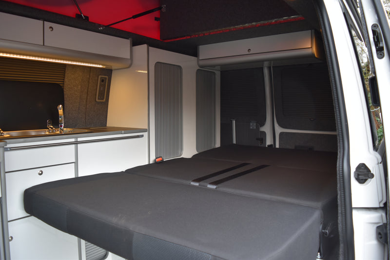 Camper interior with a grey simora RIB bed and white cabinetry