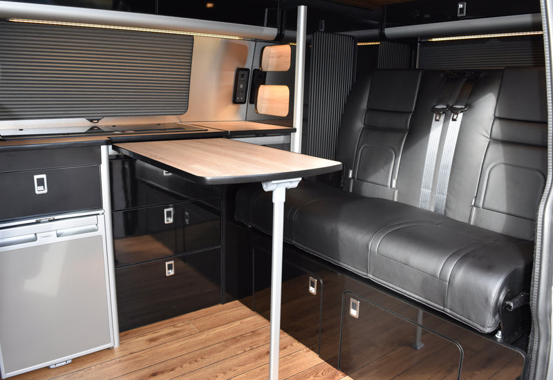 Interior of a camper van with black gloss cabinets with a wooden top, fridge and table