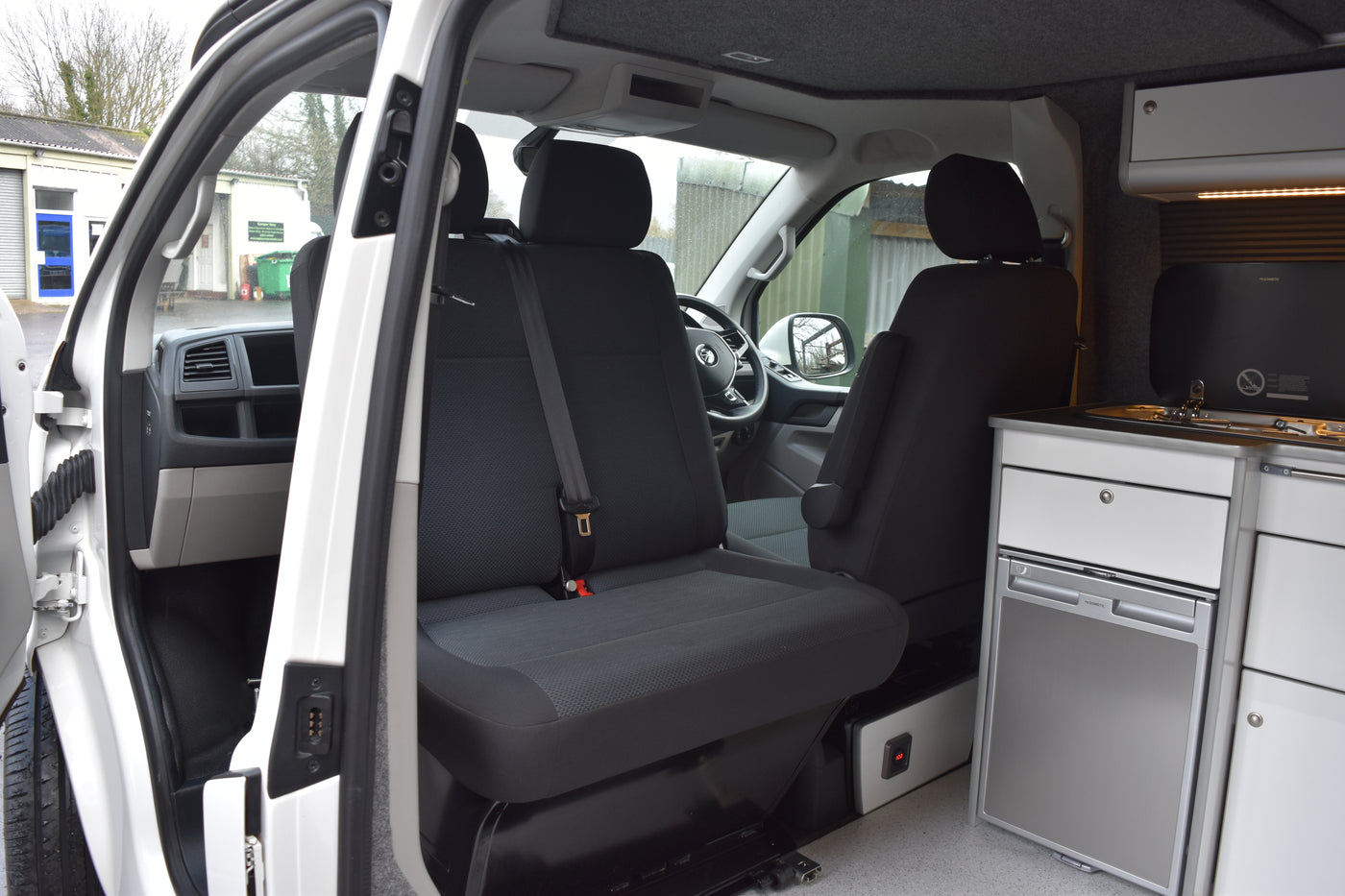 Camper van interior with black seats and a white cabinet with cooking appliances