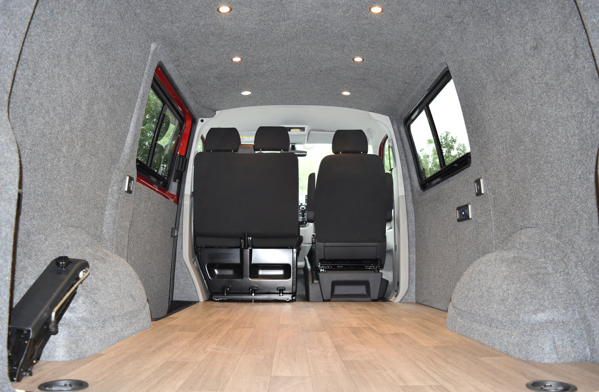 camper interior with grey carpeted walls, spot lights, electrics and windows fitted, with a wooden finished floor 
