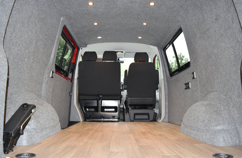 camper interior with grey carpeted walls, spot lights, electrics and windows fitted, with a wooden finished floor 