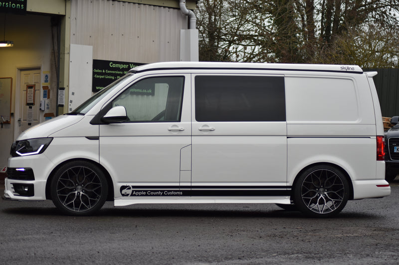 White van with a pop top and 'Apple County Customs' branding parked in front of a building.