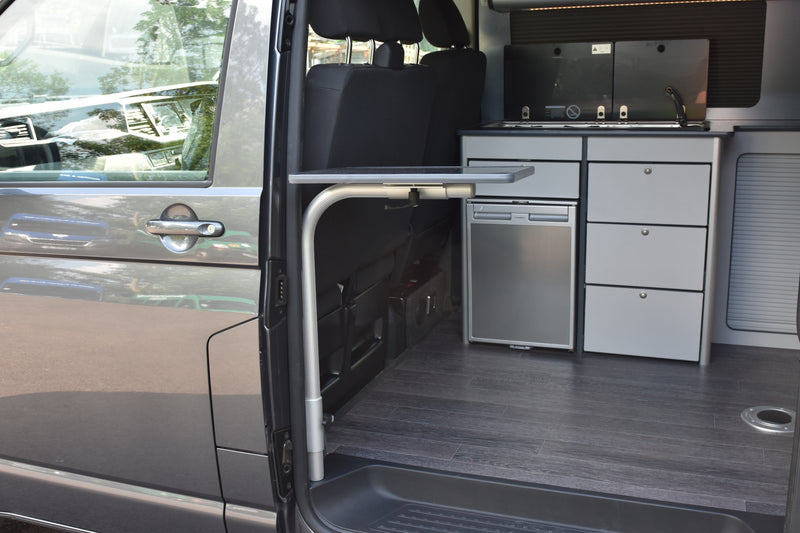 Interior of a van with kitchen setup including drawers and a refrigerator and a swing out table 
