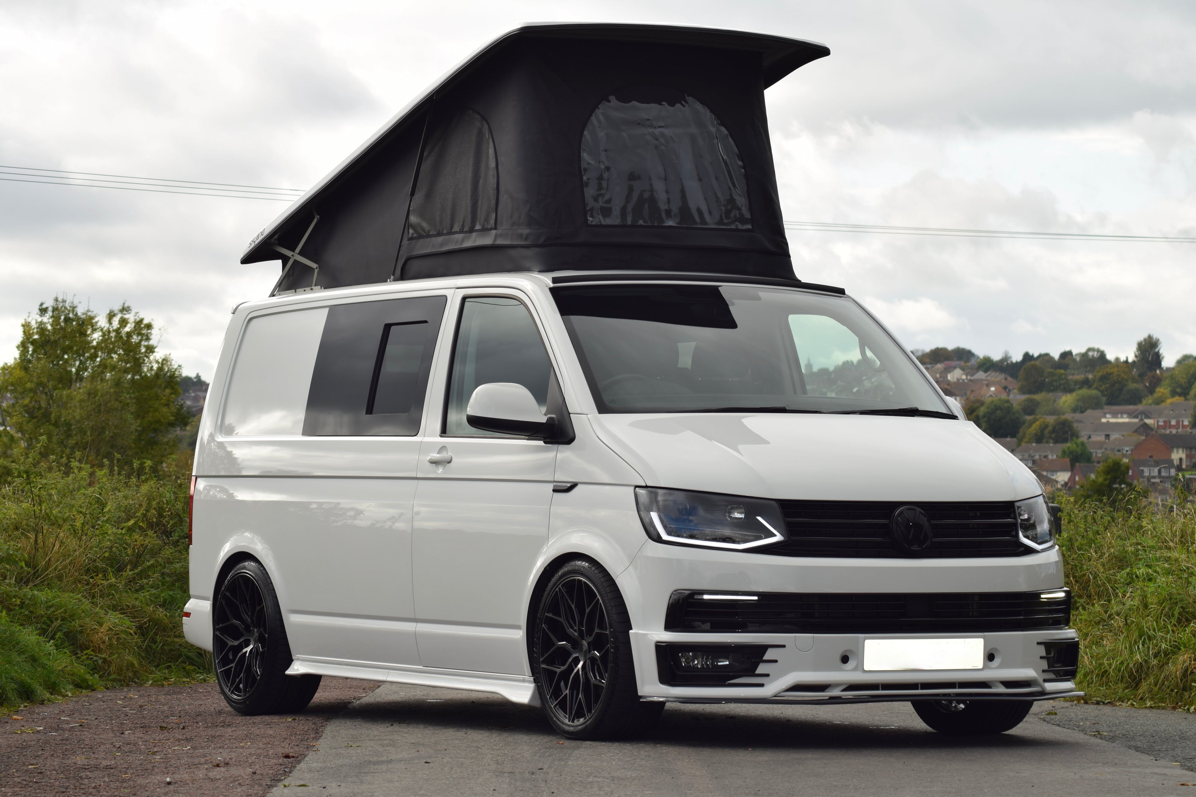 White VW Transporter camper with pop top raised, parked in an outside setting